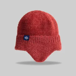 Detailed texture of thick brick red knitted beanie with snowflake patch and warm ear flaps