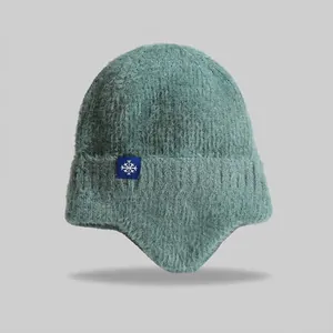 Close-up of green knitted earflap beanie with fuzzy wool texture and snowflake tag