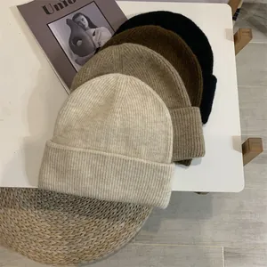 Set aus vier weichen Strickmützen in Beige, Braun und Schwarz auf einem Tisch.