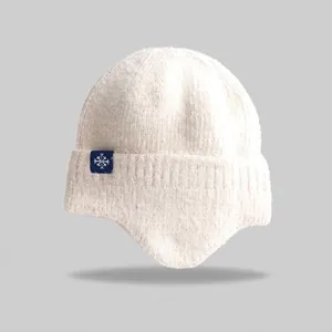Detailed macro view of the white knitted winter earflap beanie with a snowflake tag