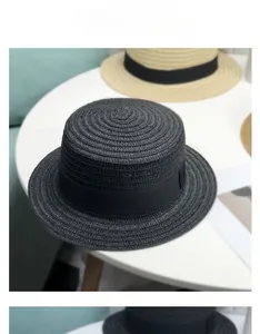 Vue détaillée d'un chapeau de paille noir à bord plat sur une table blanche élégante.