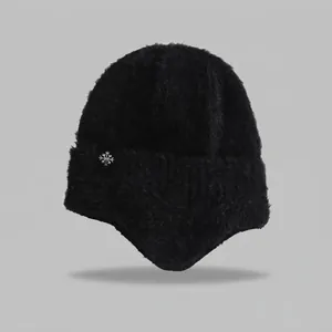 Detail view of a black fuzzy knit earflap hat featuring a small white snowflake patch