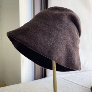 Side view of a dark brown wool slouchy bucket hat on a gold display stand
