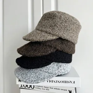 Close-up view of stacked bouclé wool newsboy caps in multiple neutral winter colors