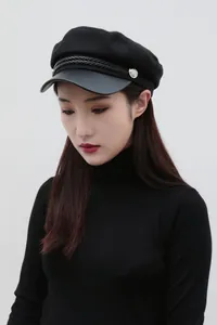 Side view of a classic black flat-top sailor hat with braided trim and silver buttons