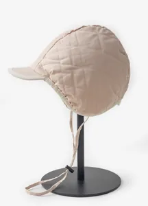 Detailansicht einer gesteppten beige Wintermütze mit Ohrenschutz und Kinnriemen.