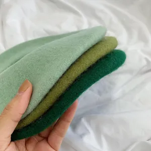 Three shades of green wool beret hats stacked in hand, showing soft texture.
