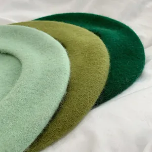 Close-up of three wool berets in a gradient of green shades on a white background.
