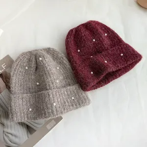 Detail of knitted beanies with pearl decorations in grey and wine red colors.