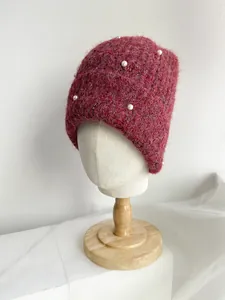 Red fuzzy knit beanie hat decorated with white pearls on a mannequin head stand