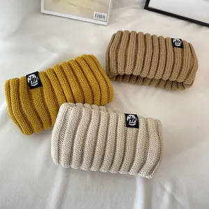 Detail view of three vintage thick knitted headbands in mustard, beige, and khaki.