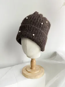 Close-up of dark brown knitted beanie with elegant pearl decorations and soft texture.