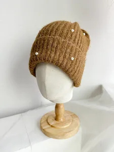 Detailed view of the brown knitted beanie featuring elegant white pearl embellishments