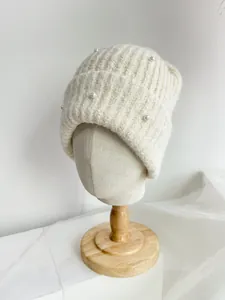Detailed view of a soft cream knitted winter beanie featuring elegant pearl embellishments.