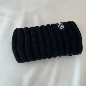 Close-up of thick black ribbed knit headband showing warm wool texture and logo tag