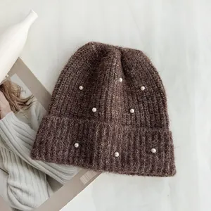 Detailed macro view of a brown knitted beanie hat featuring elegant white pearl embellishments