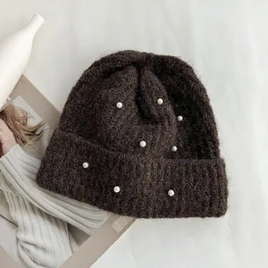 Detailed close-up of dark brown knitted beanie with elegant white pearl decorations