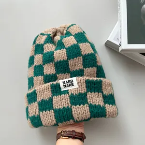 Close-up of a green and beige checkered knit beanie with a white brand label