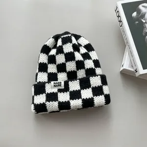 Detailed view of black and white checkered knit beanie with woven brand label.