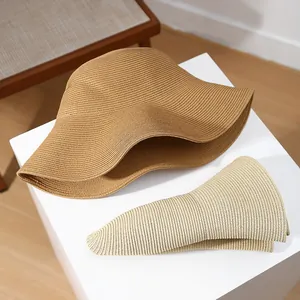 Detail view of foldable wide-brim straw sun hats in caramel and beige on a white stand