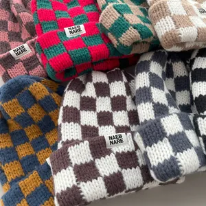 Close-up detail of thick knitted checkerboard beanies showing rich textures and multiple colors