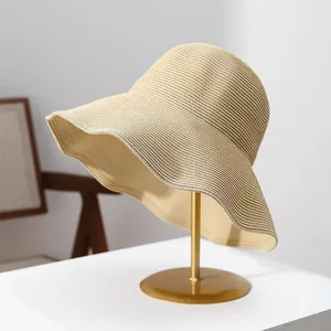 Detailed view of a woven large-brimmed straw sun hat displayed on a gold metal stand