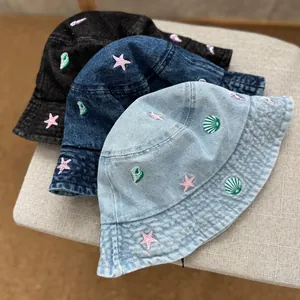 Close-up view of children's denim bucket hats in three colors with shell and starfish embroidery