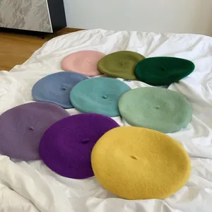 A variety of colorful solid wool beret hats displayed on a white wrinkled sheet