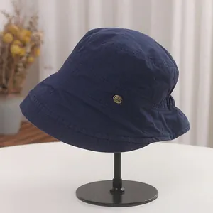 Side detail of a navy blue pleated bucket hat with a small decorative metal tag.