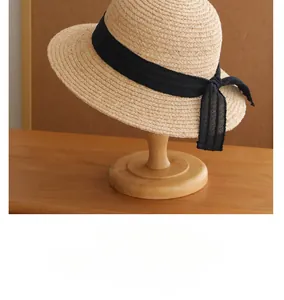 Detail of retro French straw sun hat with black ribbon bow on wooden stand.