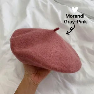 Close-up of a dusty rose wool beret held by hand against a white fabric background.