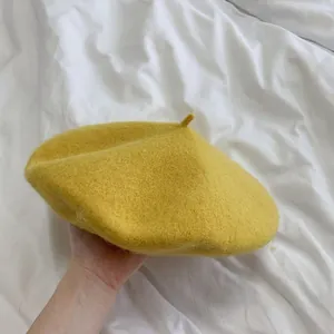 A soft chick yellow wool beret hat shown in detail on white wrinkled fabric background