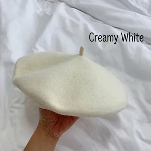 Detailed view of a classic cream white wool beret hat held against white bedding.
