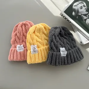 Primo piano di berretti in maglia a treccia rosa, gialli e grigi con etichette.