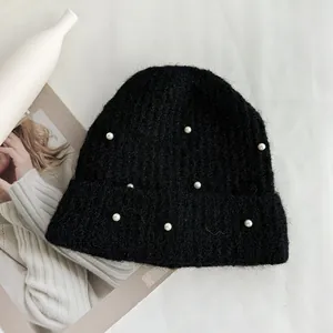 Detailed macro shot of a black knitted beanie hat with elegant white pearl bead decorations