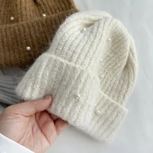 Close-up detail of soft white knit beanie with elegant white pearl bead decorations.