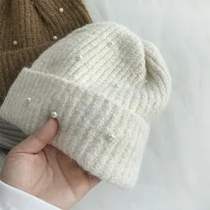 Close-up of a white winter knitted beanie decorated with elegant pearls and soft texture.