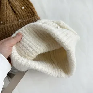 Detailed view of white knitted winter hat showing thick warm lining and pearl decor