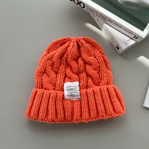 Dettaglio di un berretto invernale arancione in maglia a trecce con toppa in tessuto bianco