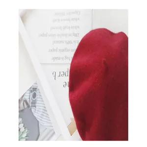 Close-up detail of a classic red wool beret on minimalist paper bag backdrop