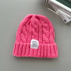Berretto in maglia a trecce rosa acceso con etichetta tessuta su sfondo minimalista.