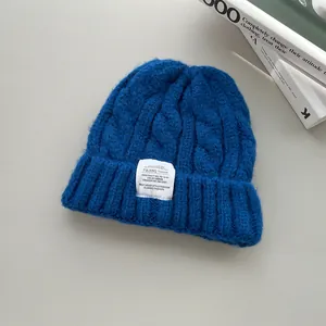 Dettaglio berretto blu in maglia a trecce con toppa bianca su sfondo grigio