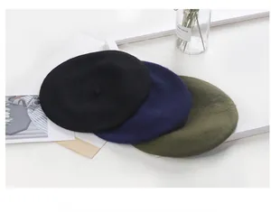 Three classic winter wool berets in black navy and olive green on white tabletop