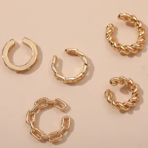 Close-up of multiple gold twisted and chain link cuff earrings on a beige background