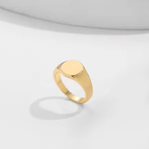 Close-up detail of a minimalist gold-colored signet ring with a smooth circular top.