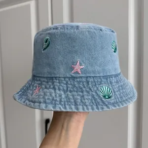 Detailed close-up of shell and starfish embroidery on a blue denim bucket sun hat