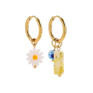 Close-up of asymmetric gold hoop earrings with white daisy and yellow stone charms