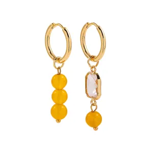 Detailed macro view of asymmetrical gold-plated hoop earrings with yellow beads and clear crystal.