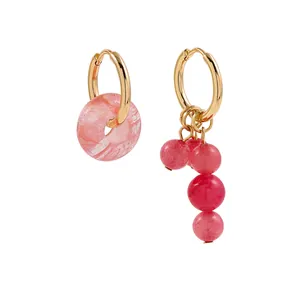 Macro view of asymmetric gold-tone hoop earrings with pink marble donut and beaded charms.