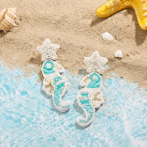 Detailed close-up of handmade beaded seahorse earrings with starfish studs on sand.